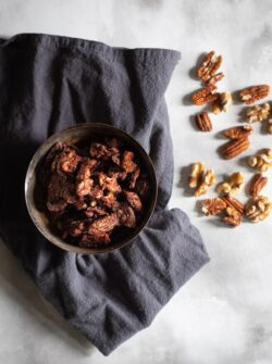 candied pecans and walnuts in a bowl with grey cloth