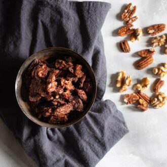 candied pecans and walnuts in a bowl with grey cloth