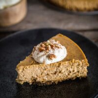 a slice of pumpkin spice cheesecake with whipped cream and pecans on top.