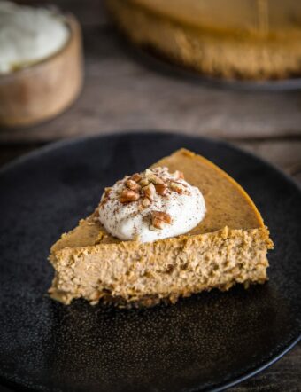 a slice of pumpkin spice cheesecake with whipped cream and pecans on top.