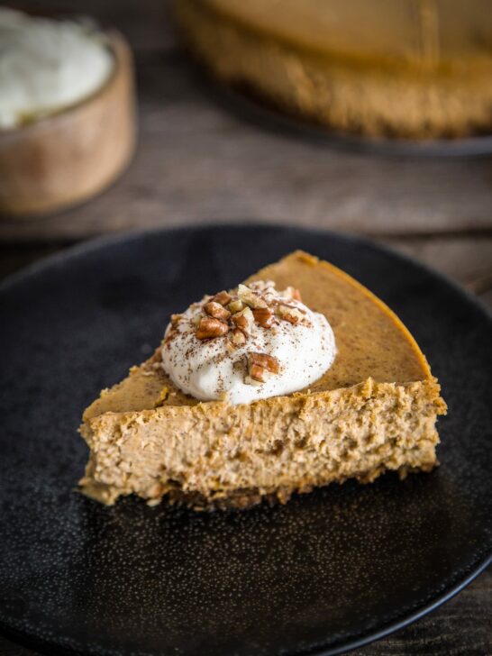 a slice of pumpkin spice cheesecake with whipped cream and pecans on top.