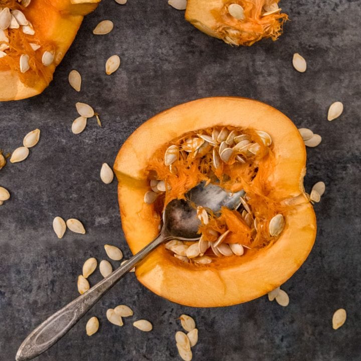 Two pumpkin halves face up exposing seeds with spoon and stem