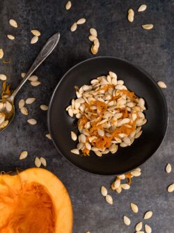 Black bowl with pumpkin seeds and pumpkin half face up