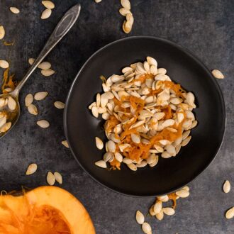 Black bowl with pumpkin seeds and pumpkin half face up