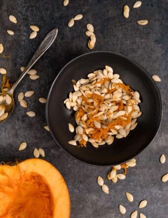 Black bowl with pumpkin seeds and pumpkin half face up