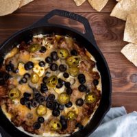 taco dip in cast iron skillet with olives, jalapenos, and chips