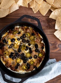 taco dip in cast iron skillet with olives, jalapenos, and chips