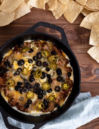 taco dip in cast iron skillet with olives, jalapenos, and chips