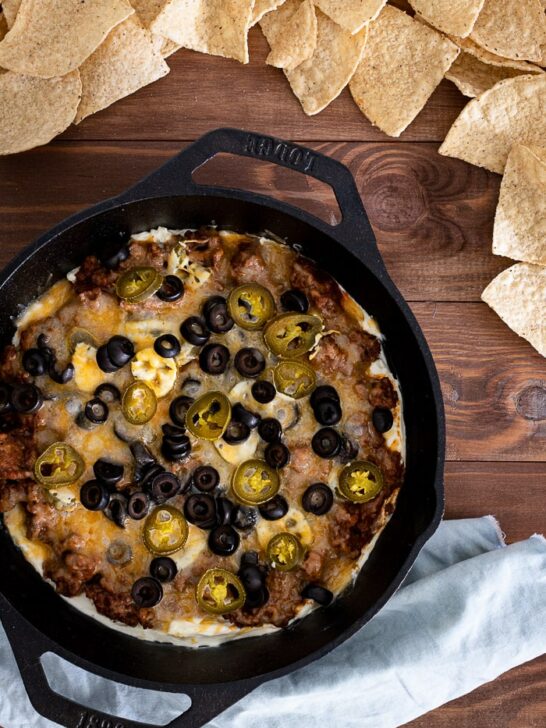 taco dip in cast iron skillet with olives, jalapenos, and chips